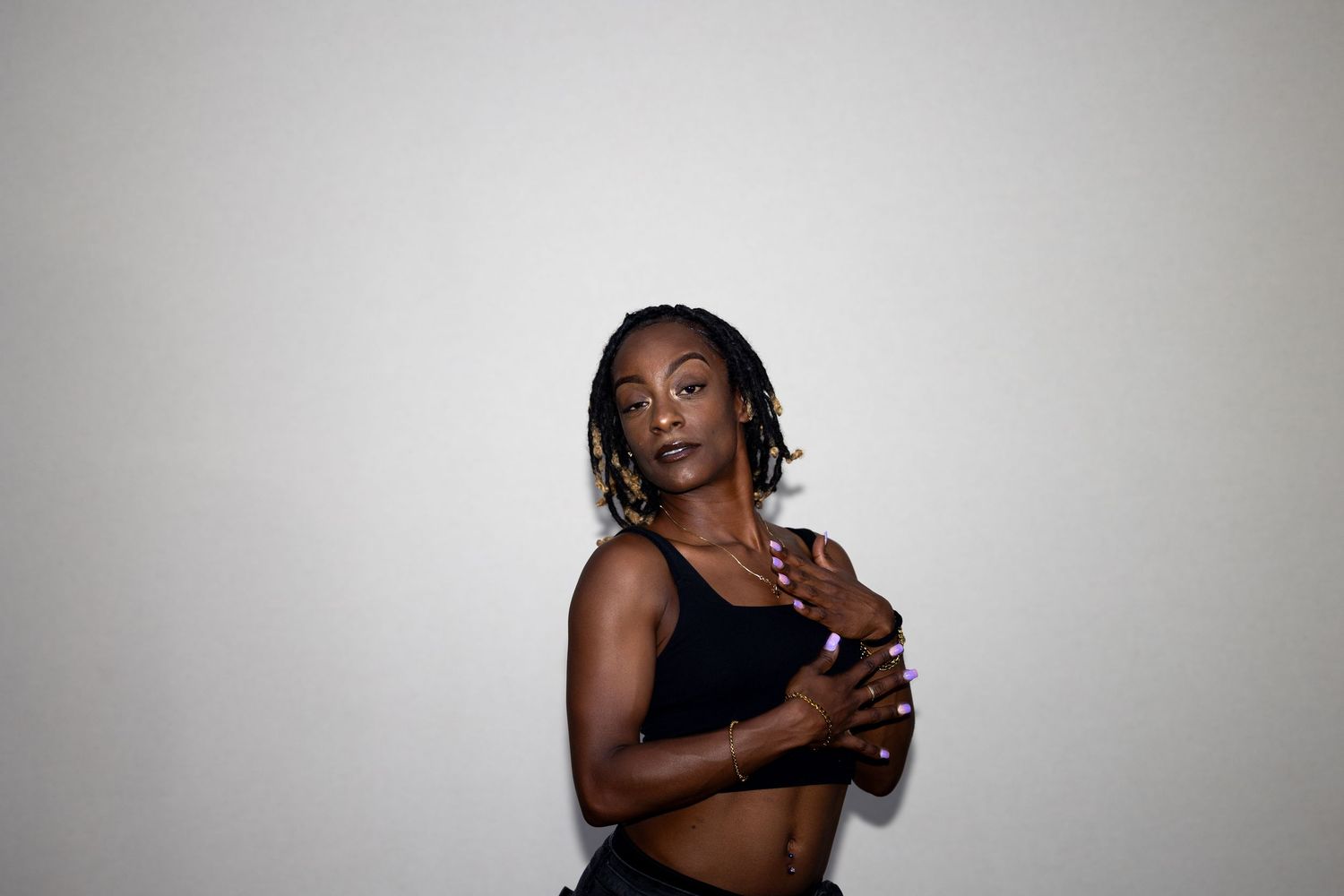 Athletic young woman with braids in a black crop top crossing her arms against a white background.