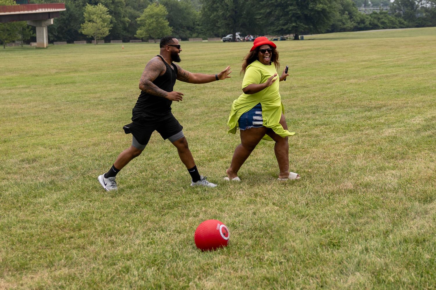 Two people playing with a red ball on a grassy field during an outdoor summer game day.