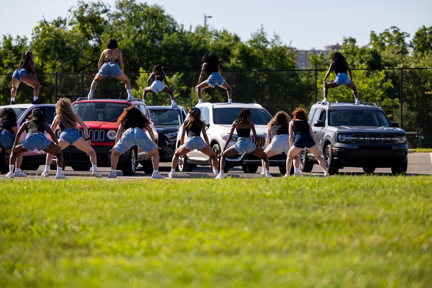 Cheerleaders performing synchronized routine outdoors near parked trucks on a sunny day.