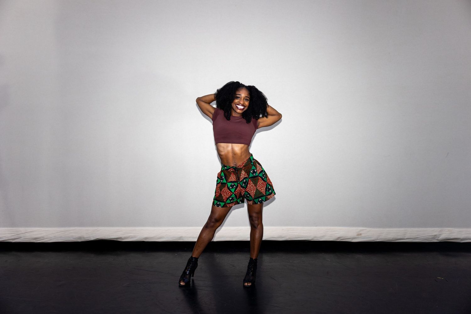 Woman in mauve crop top and colorful African print mini skirt posing against a light gray background.