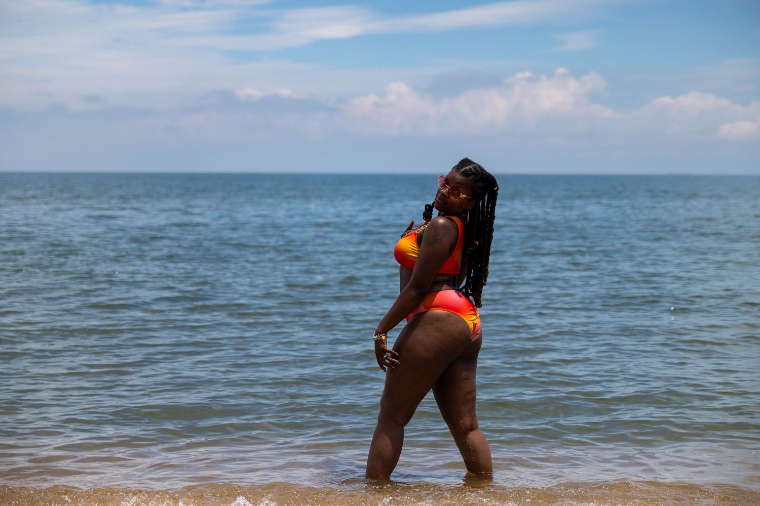 Woman in colorful bikini posing on beach shoreline with ocean waves and blue sky background.