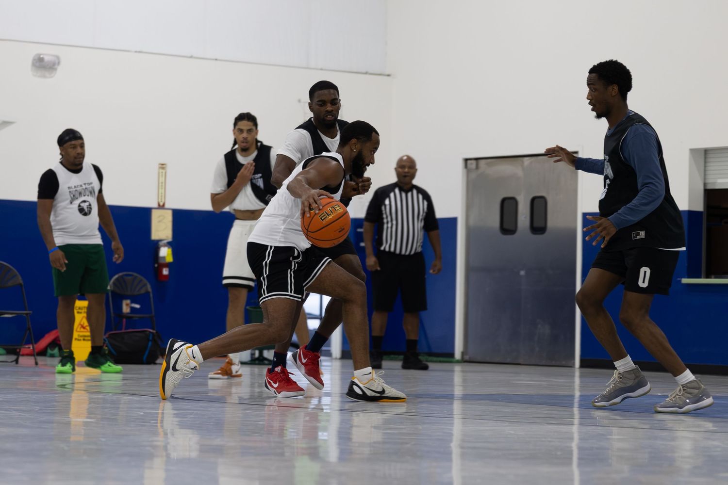 Young men playing competitive indoor basketball game on a court with a referee watching nearby.