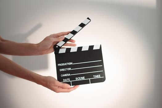 Hands holding a black film clapperboard with white text on a light background for movie production.
