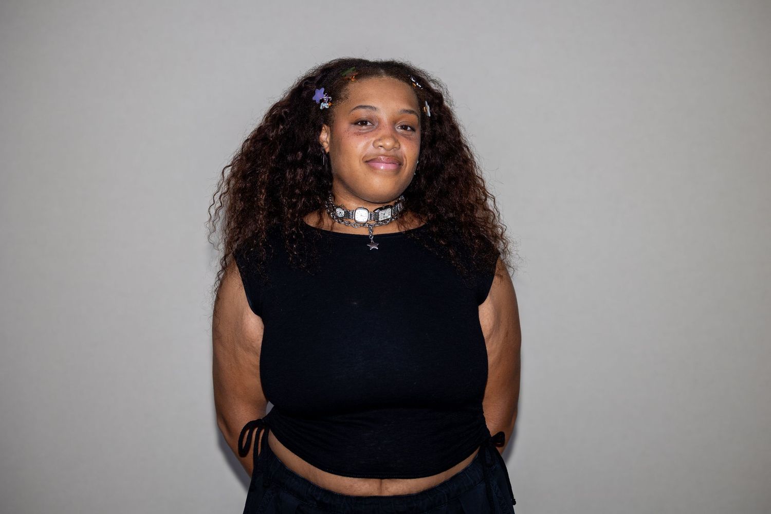 Young woman with curly hair wearing black crop top and studded choker necklace posing confidently.