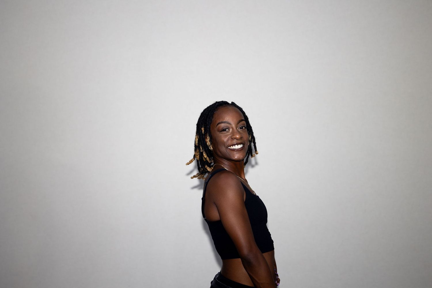 A slim woman in a black crop top laughs over her shoulder against a bright white background.