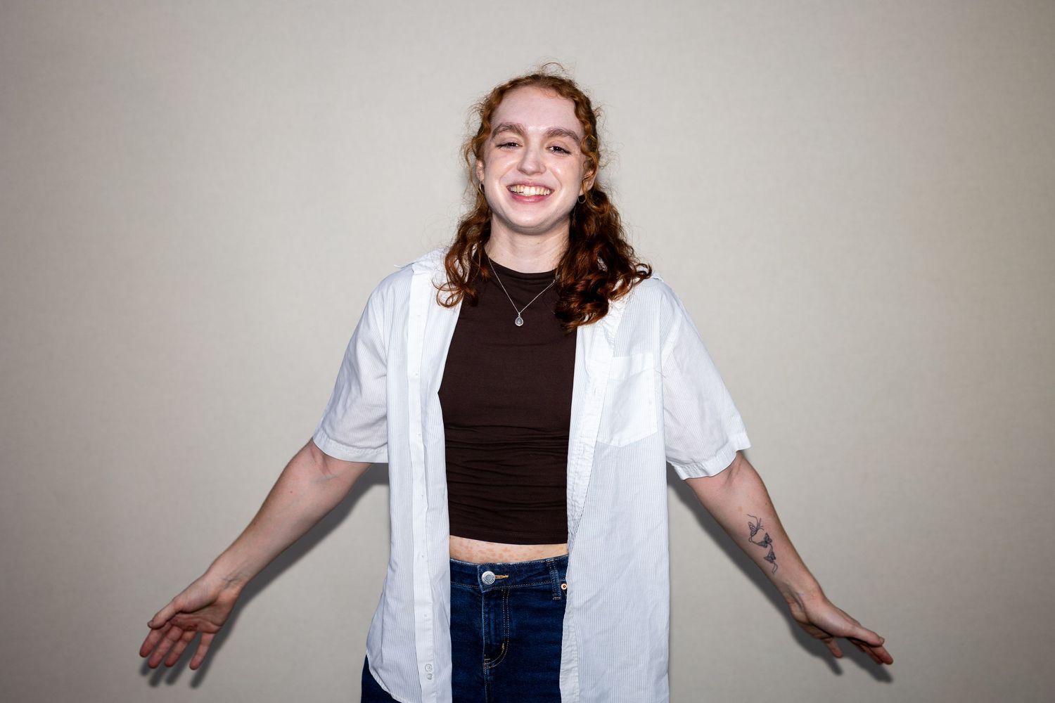 Smiling redhead woman in white shirt and jeans posing with arms spread wide.