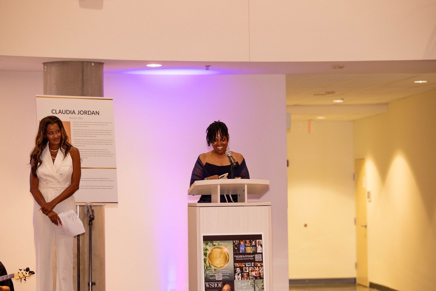 Woman speaking at podium during Claudia Jordan event in modern venue.