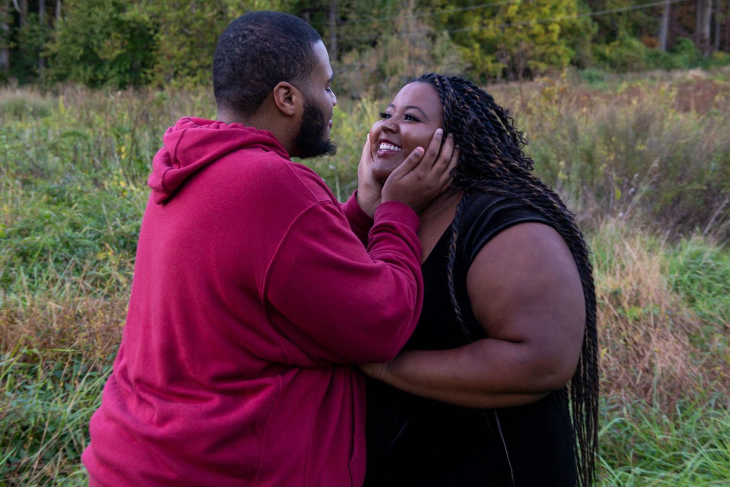 Happy couple sharing a romantic moment outdoors, man in red hoodie tenderly holding woman's face.