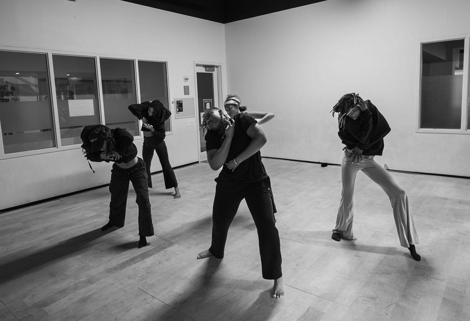 Black and white photo of four dancers performing dynamic movements in a modern studio space.