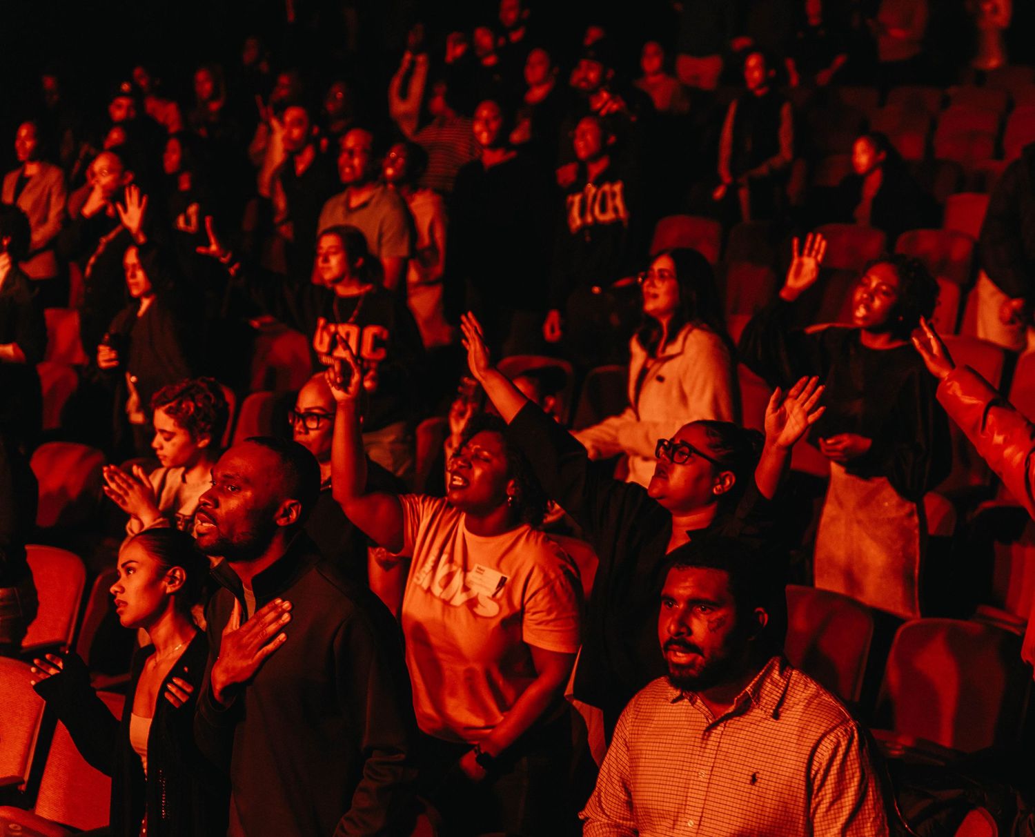 Crowd of concertgoers bathed in dramatic red lighting at a music event.