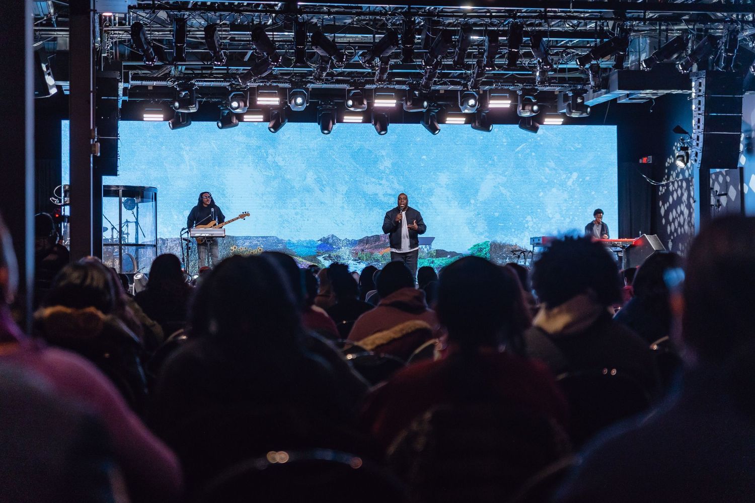 Concert crowd silhouettes against bright stage lights during a live performance at night.