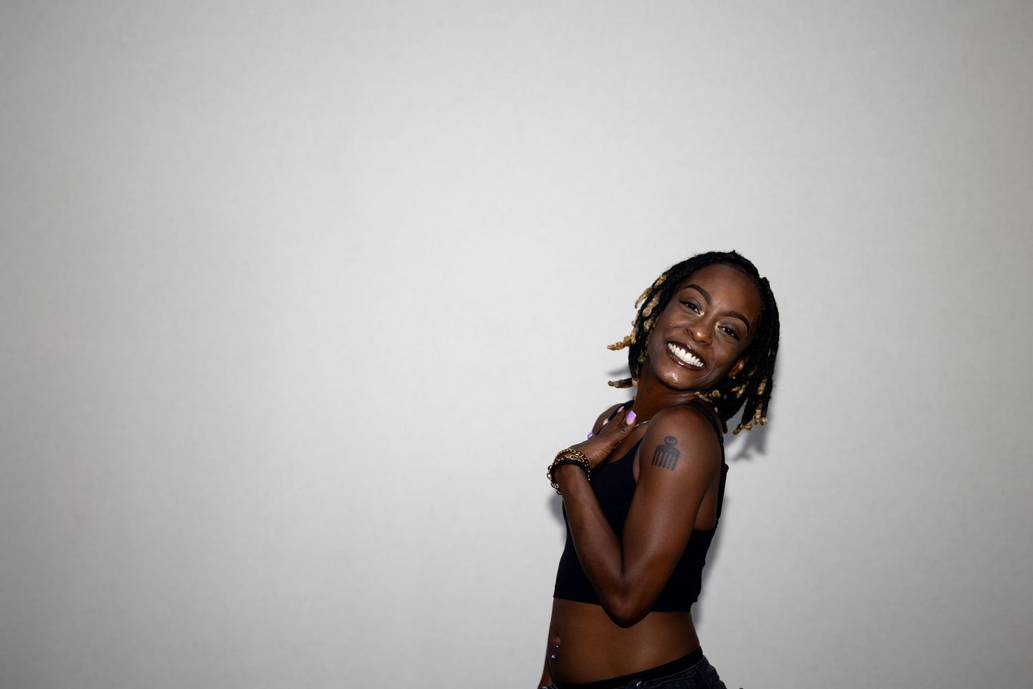 A joyful young woman in a black crop top laughs and poses against a bright white background.