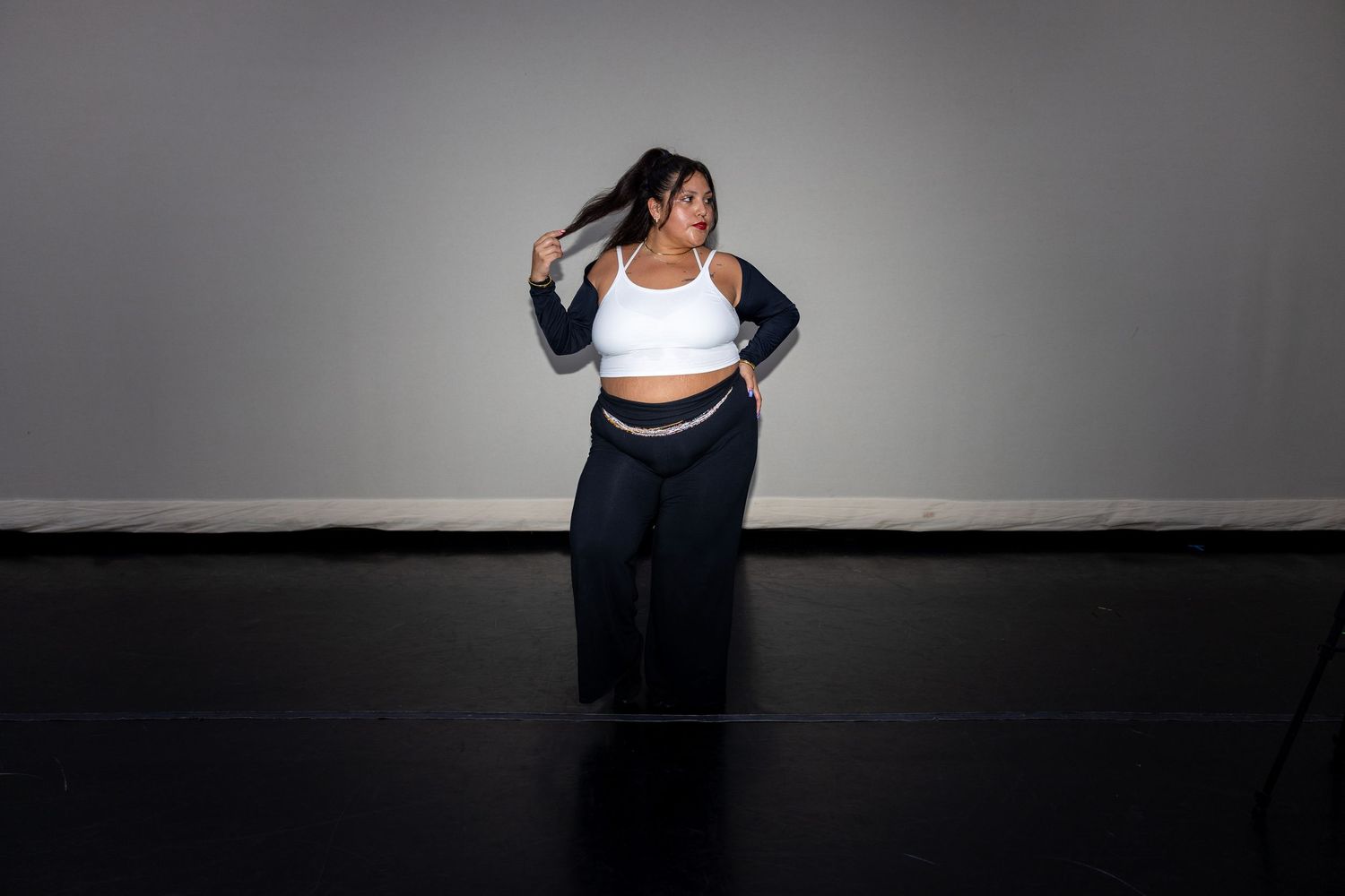Woman in white crop top and navy wide-leg pants dancing expressively in a studio space.