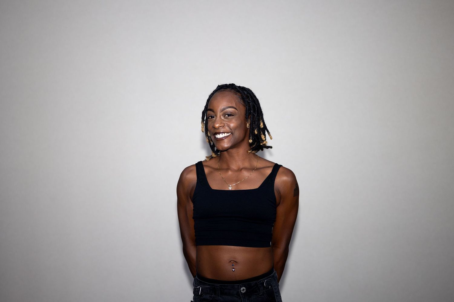 Smiling young Black woman with braids wearing a black crop top posing against a light gray background.