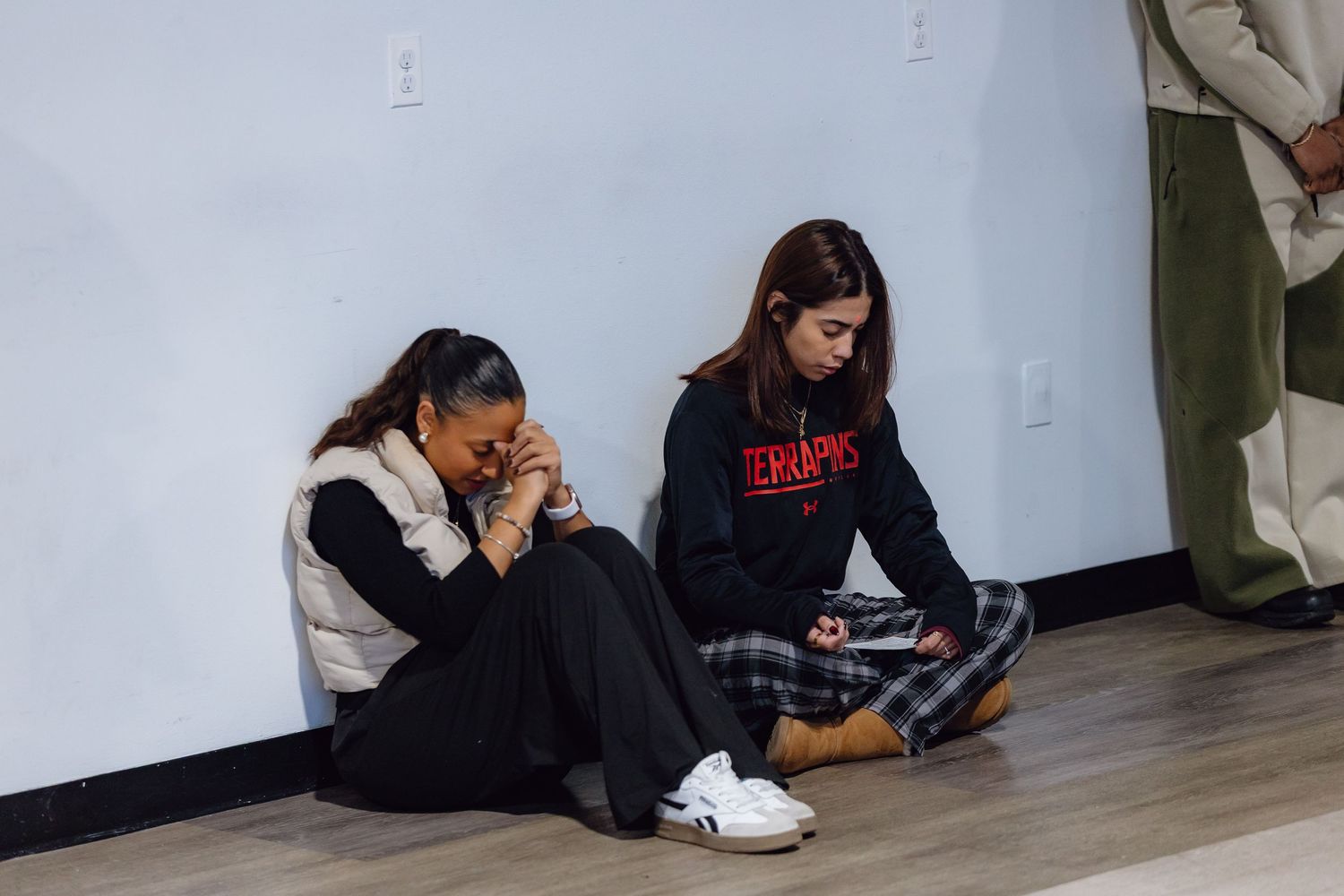 Students sitting on floor against wall studying and reading books in school hallway.