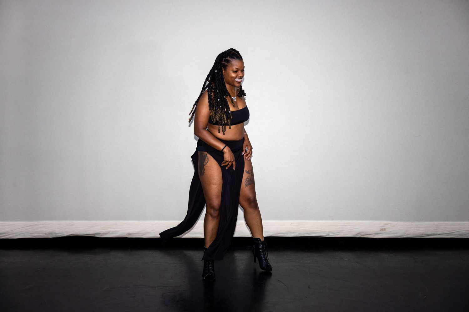 A dancer in black sequin bralette and flowing skirt strikes a dramatic pose on a dark floor.