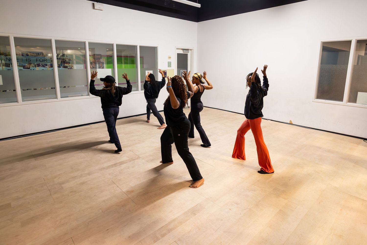 Group of dancers rehearsing contemporary choreography in a bright studio with mirrored walls.