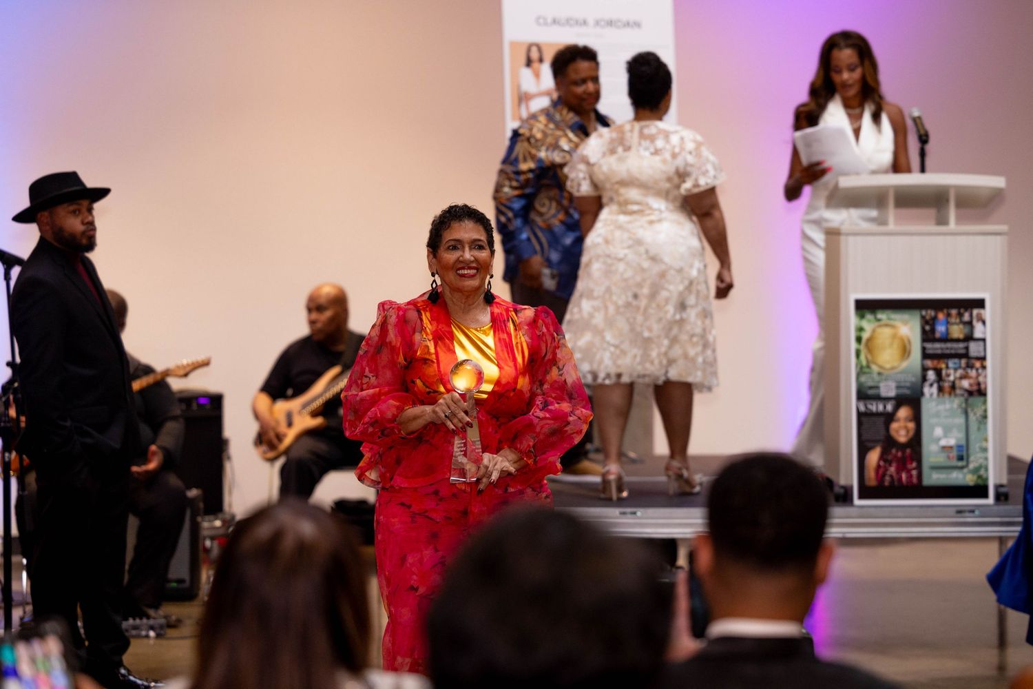 Woman in red outfit accepts award on stage at Women Songwriters Hall of Fame event with live band.