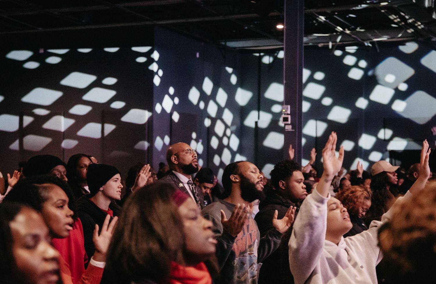 A crowd of people raise their hands in worship during a church service or religious gathering.