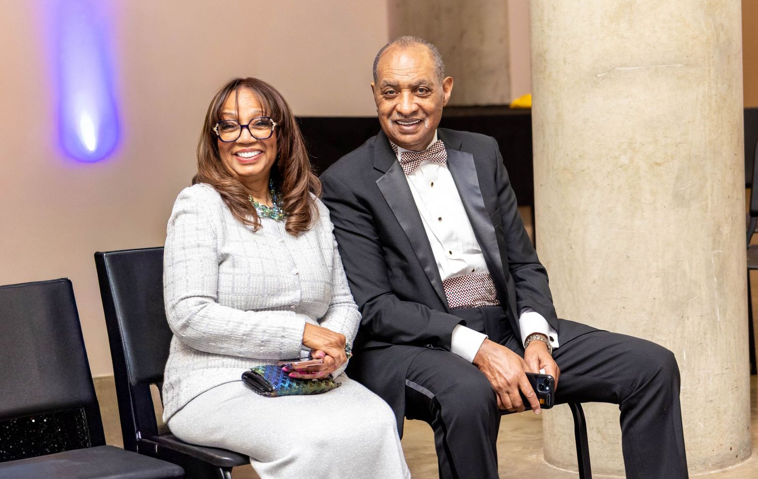 Two elegantly dressed individuals sitting together at a formal event, smiling for a photo.
