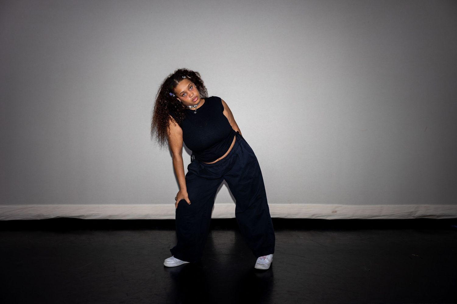 A dancer in black wide-leg pants and crop top strikes a dynamic pose against a gray studio backdrop.