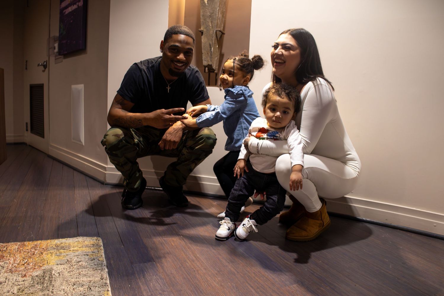 Happy family with two young children posing together in a modern hallway with wood floors.