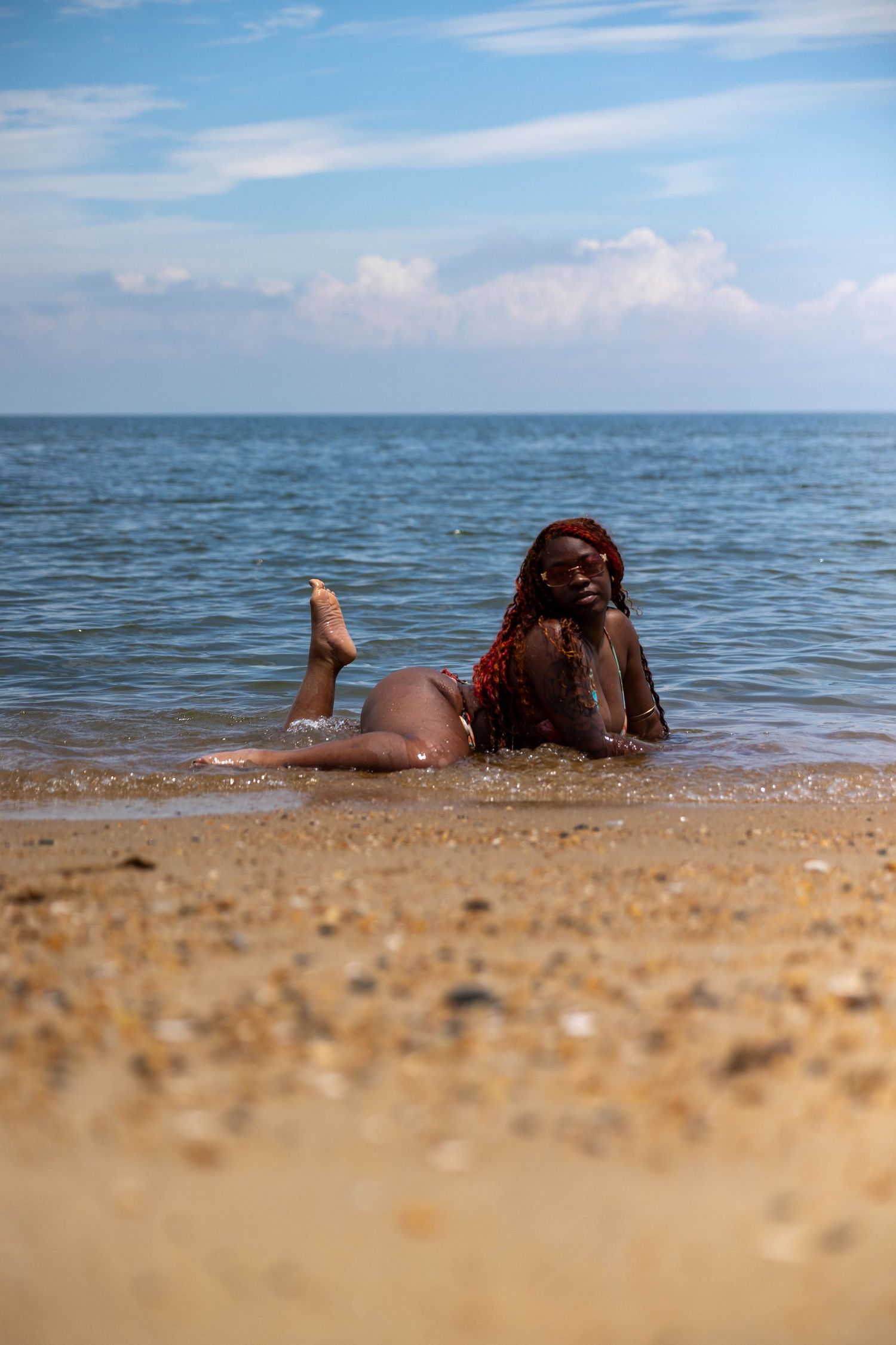 A woman in a red bikini lies on a sandy beach shore with ocean waves behind her.