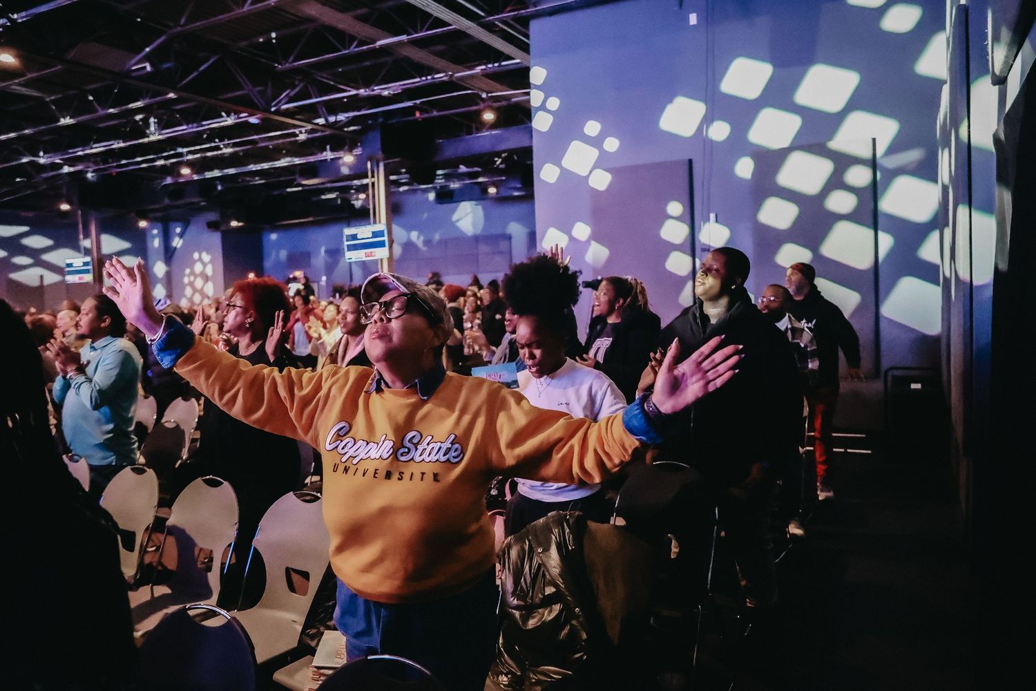 A crowded gaming convention floor shows attendees playing games at multiple stations with blue lighting and displays.