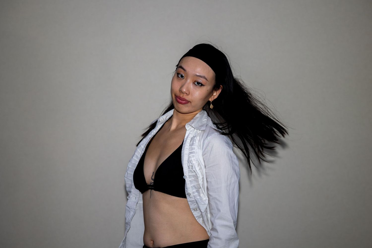 An Asian woman with long dark hair tosses her hair wearing a black bikini top and white jacket.