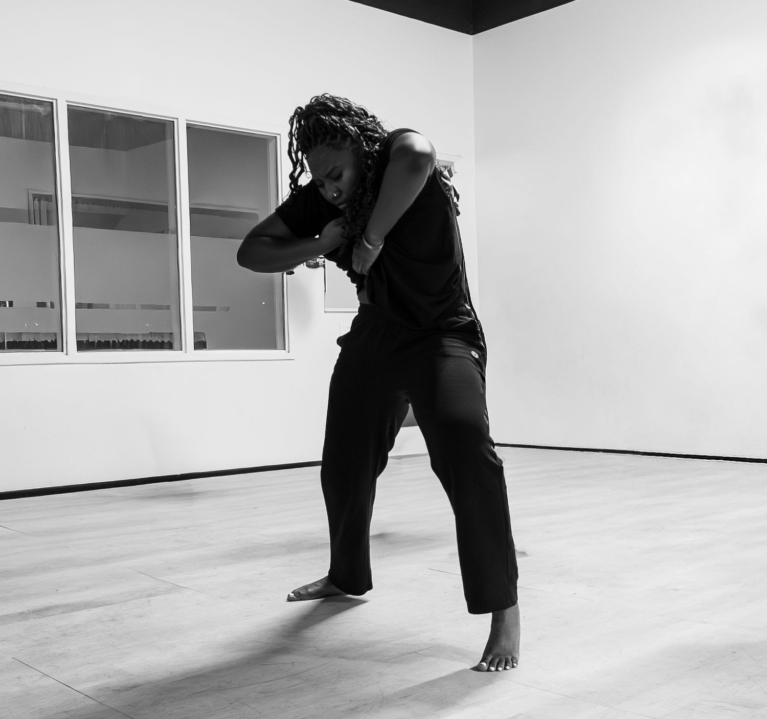 A solo dancer in black attire performs an expressive contemporary dance move in a minimalist studio.