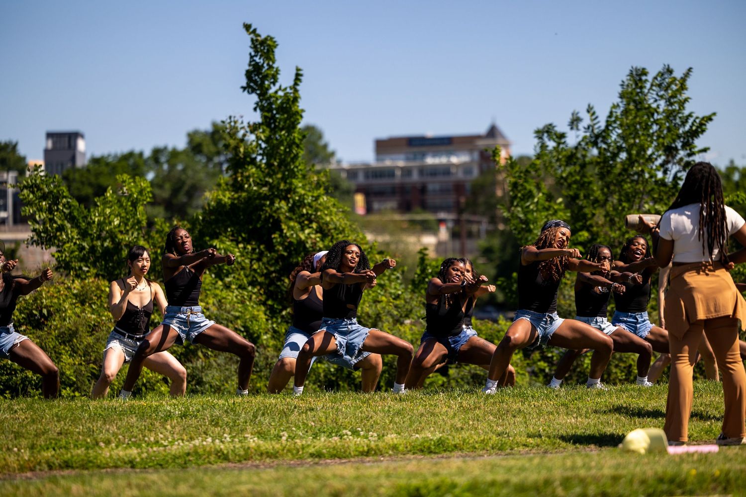 Group of young women performing a synchronized dance routine outdoors in a park on a sunny day.