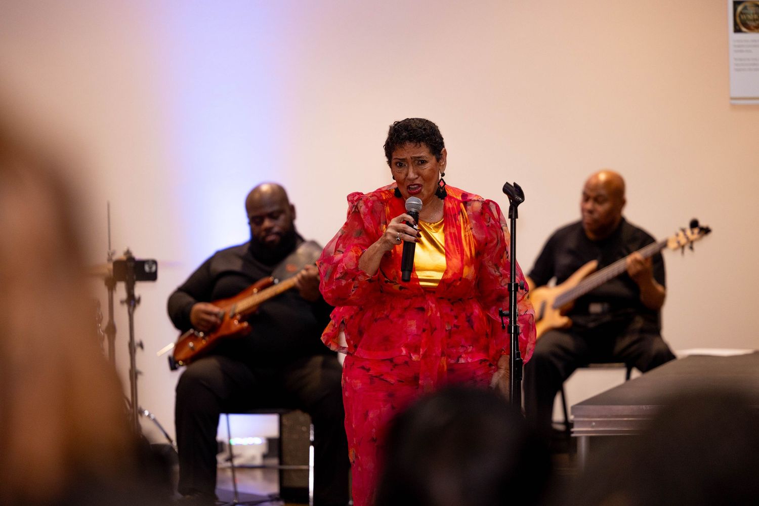 Female vocalist in red performs with live band at Women Songwriters Hall of Fame indoor event.