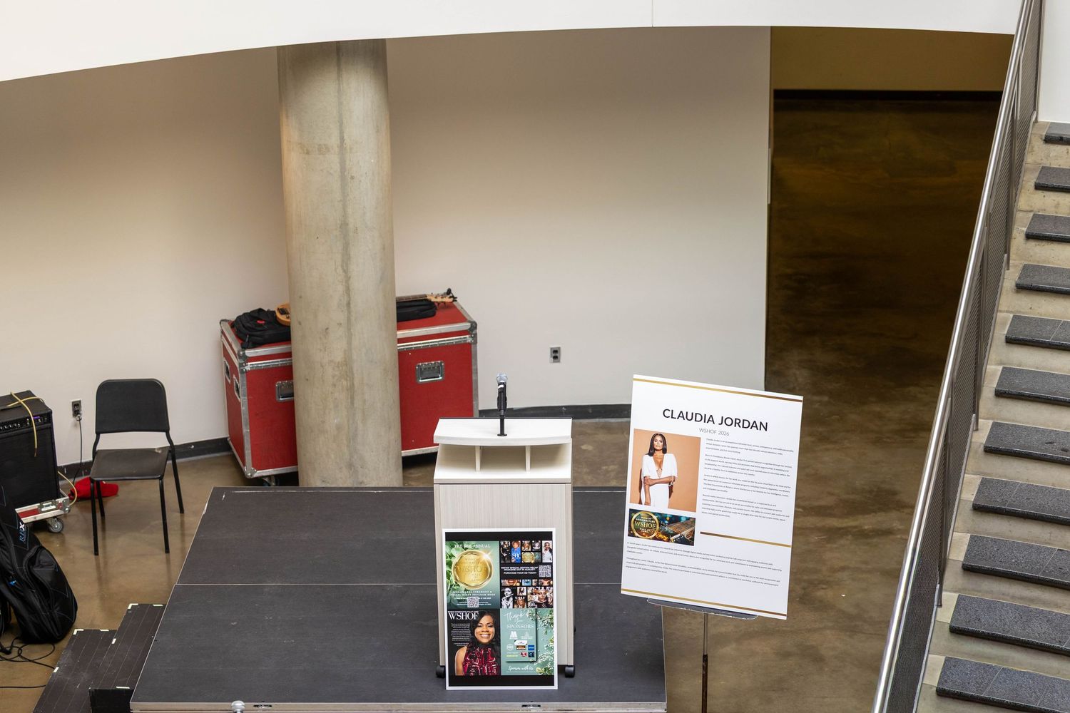 Indoor venue display with Claudia Jordan sign, podium, chairs, red equipment cases, and staircase.