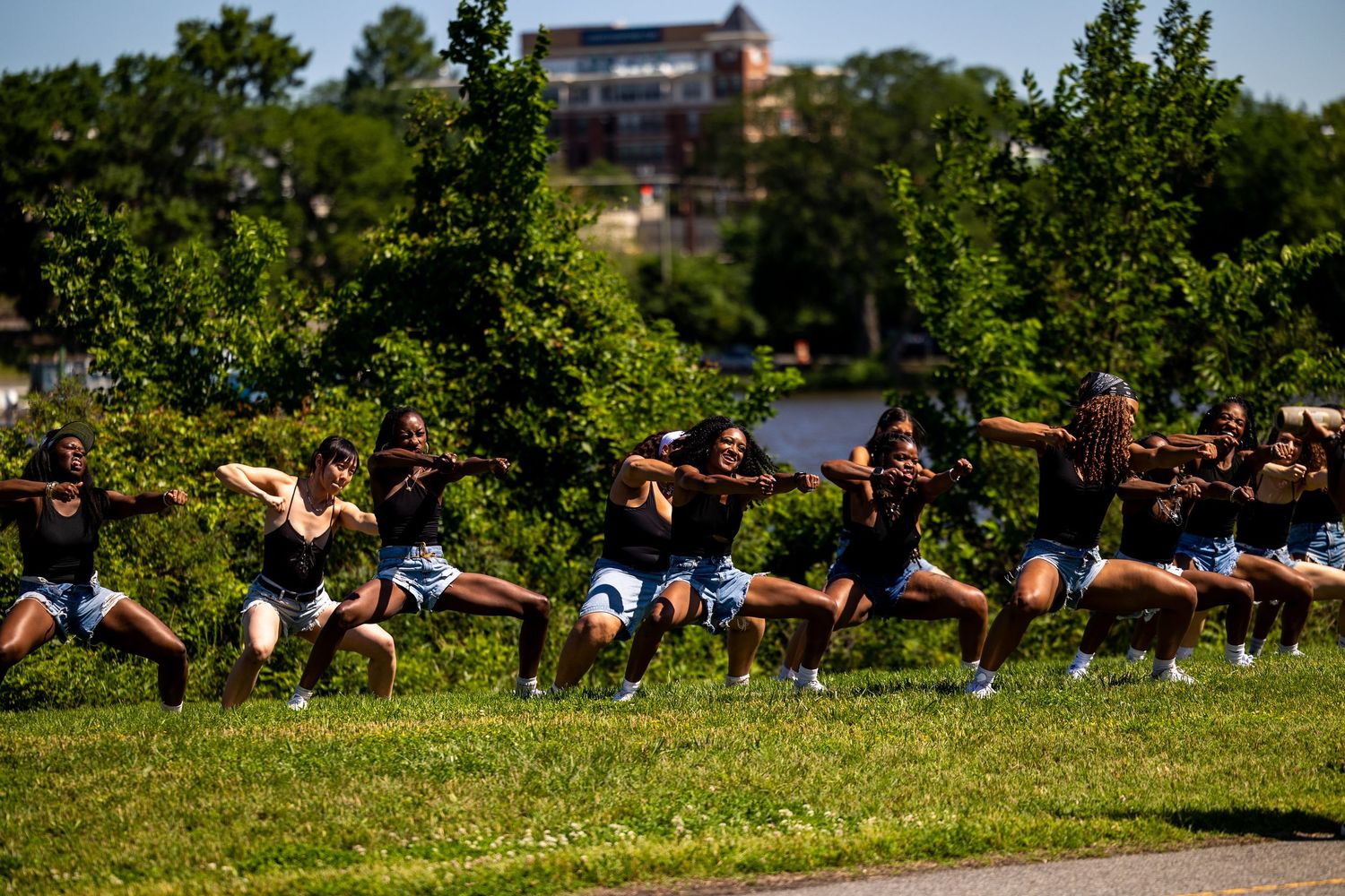 A synchronized dance team performs an outdoor routine in black tops and blue shorts on a green lawn.