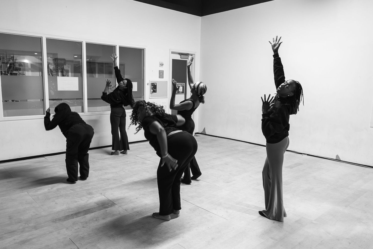 Black and white photo of modern dancers in expressive poses reaching upward in a white studio.