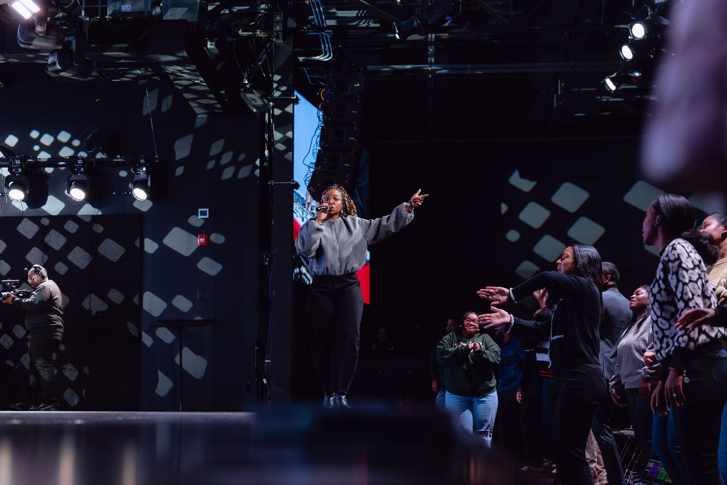 A high-energy concert performance on stage with dramatic lighting and a crowd of spectators in the background.