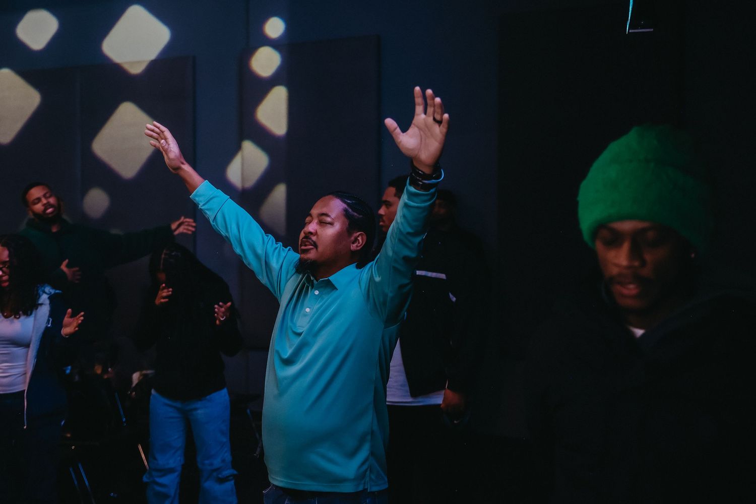 A person in a light blue sweater raises their arms in celebration at a dark nighttime event with others in the background.