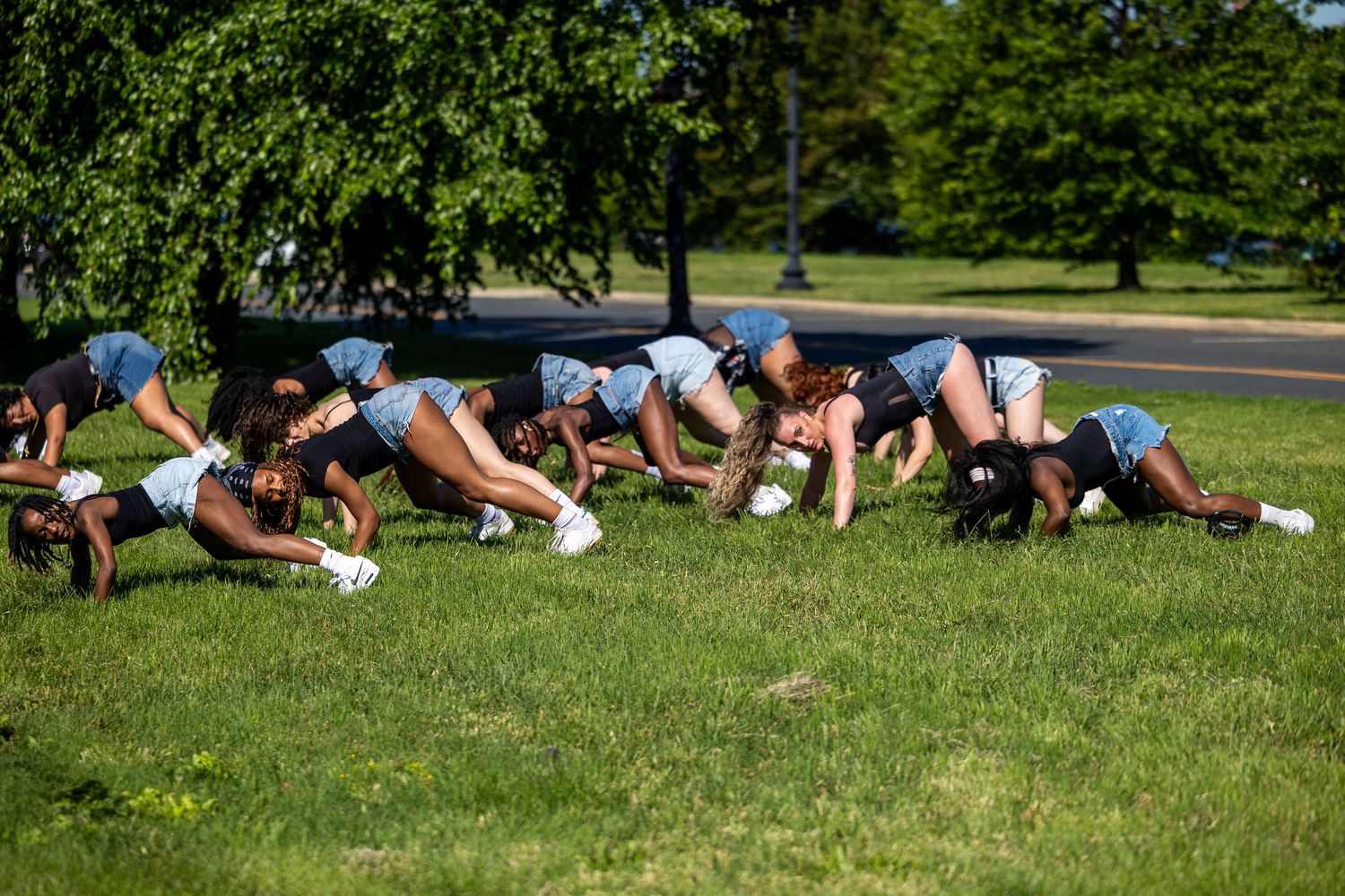 A group of young women in matching outfits doing push-ups on green grass in a park.