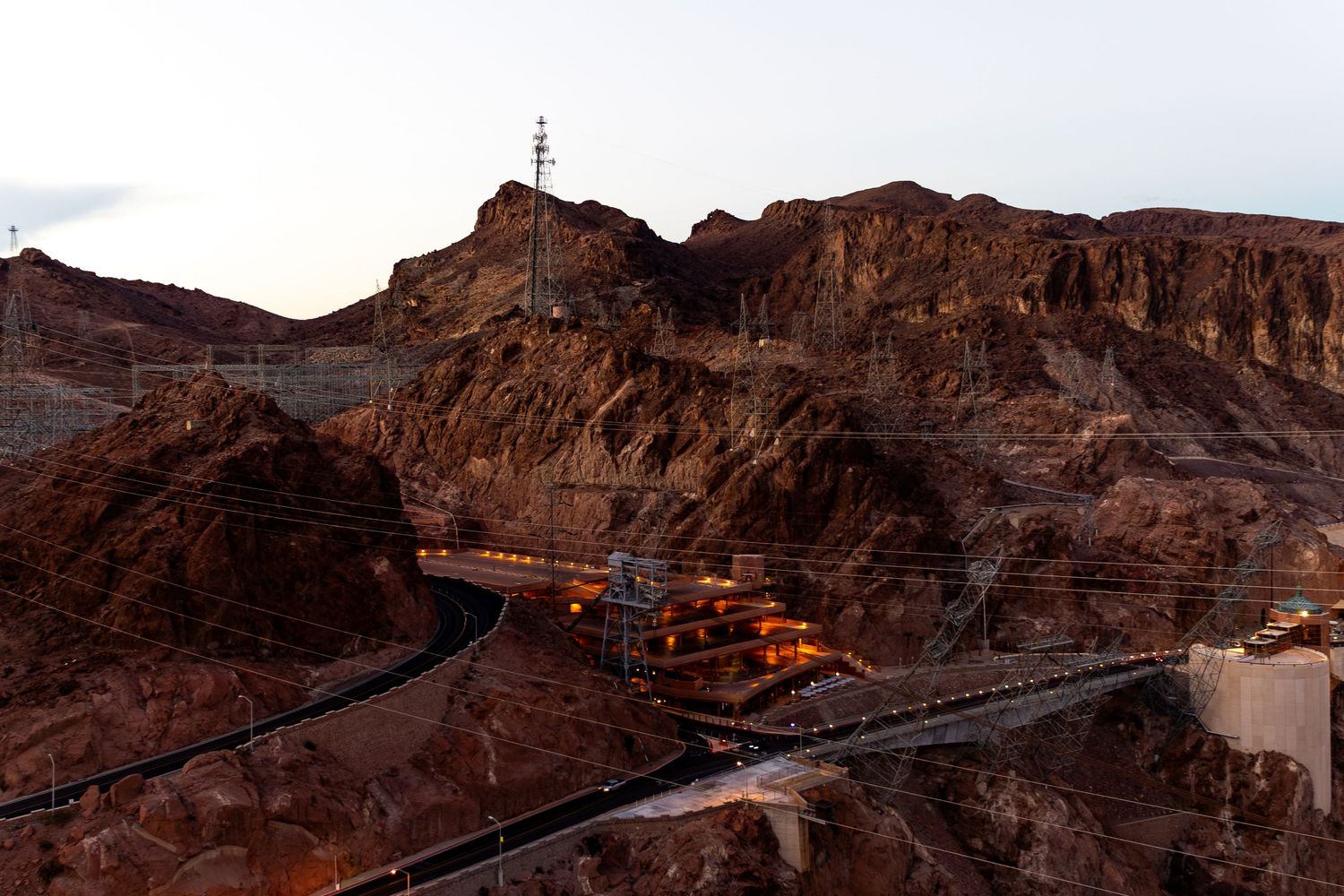 Scenic view of winding roads through red rock canyons at dusk with glowing lights along the mountainside.