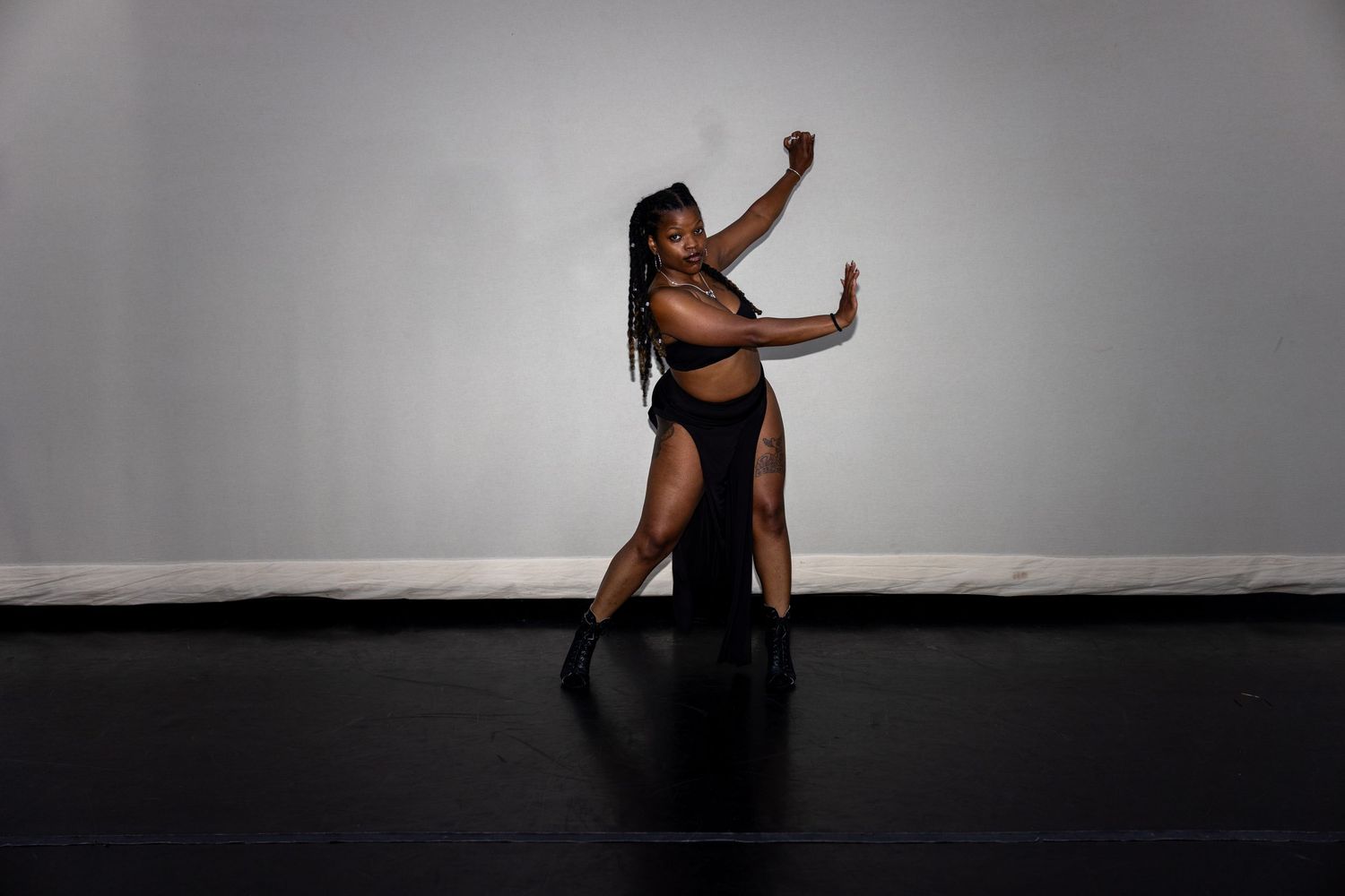 A dancer in a black outfit strikes a dramatic pose on a dark stage floor.
