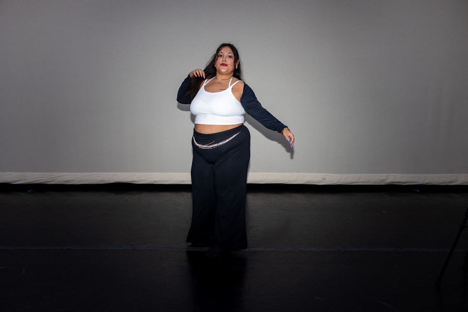 Plus-size woman dancing in white crop top and navy blue wide-leg pants against gray studio wall.