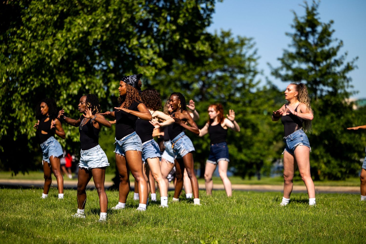 Young women dancing outdoors on green grass with trees in background on a sunny day.