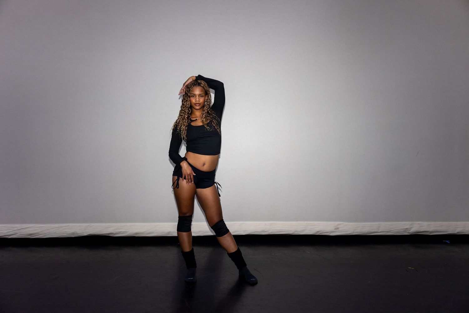 Dancer in black outfit striking a dramatic pose in a professional studio setting.