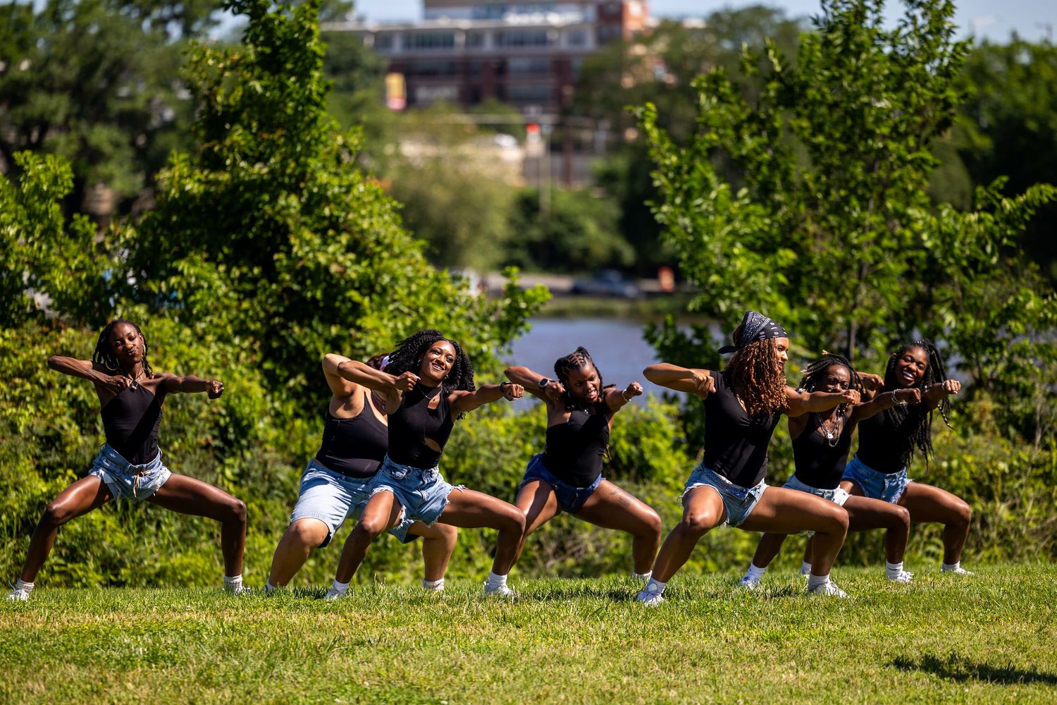A group of young women in matching outfits perform a synchronized dance routine on a grassy lawn outdoors.