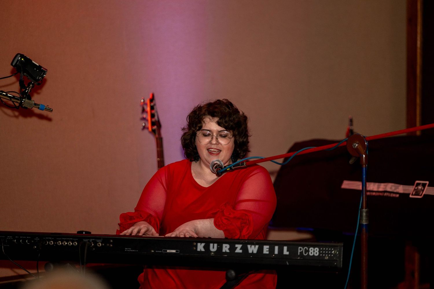 Woman in red dress playing Kurzweil PC88 keyboard on stage, smiling while performing live music.