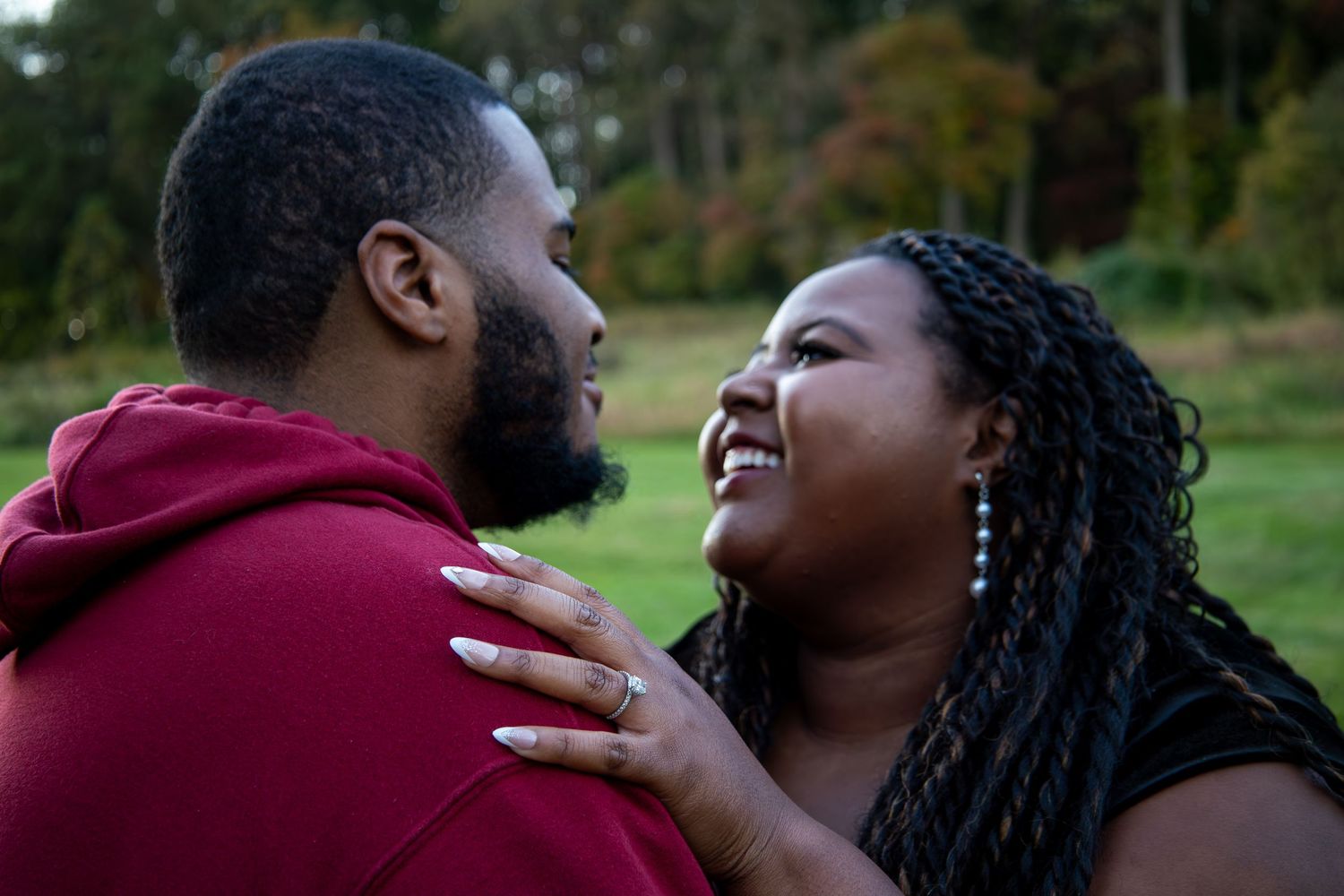 A romantic couple sharing intimate moments in burgundy attire against a natural outdoor setting.