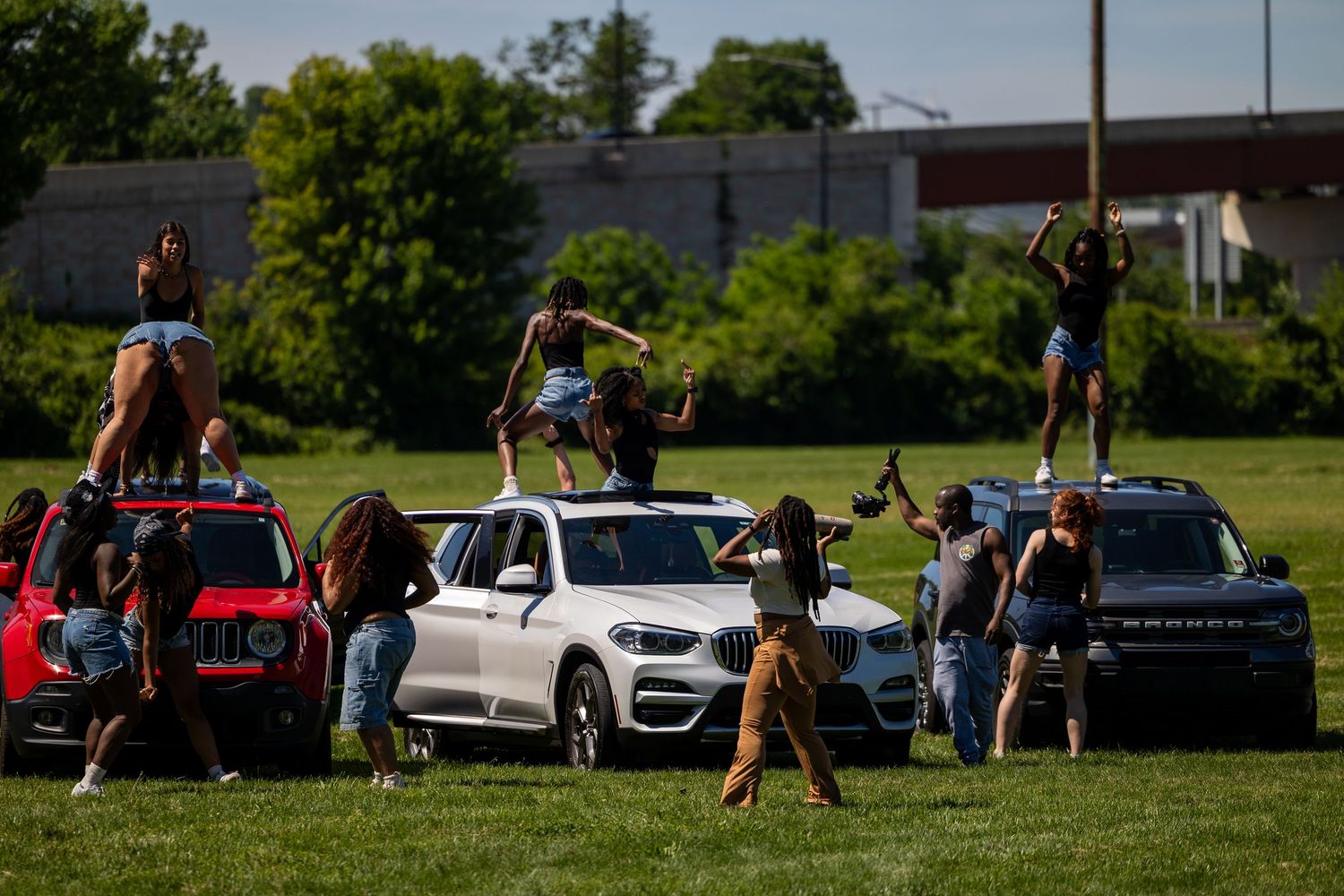 People dancing on top of SUVs parked on a green field on a sunny day.