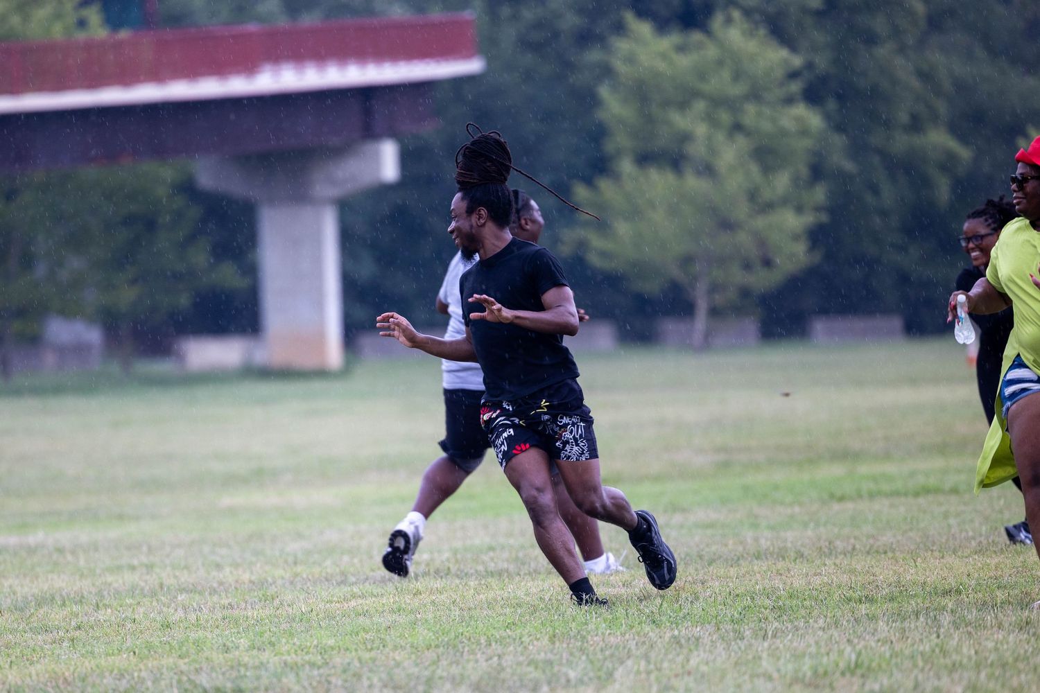 Two athletes compete in a flag football game on a green grass field with a bridge visible in the background.