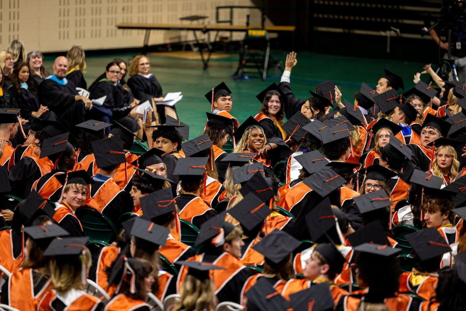 Crowd of graduates in black caps and orange regalia celebrate at a university commencement ceremony.