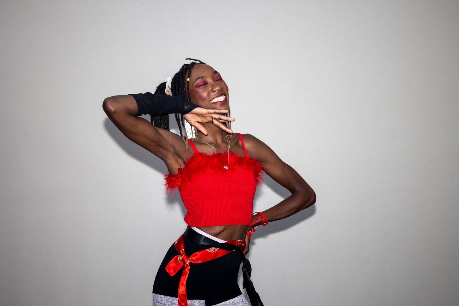 Young woman in red feathered crop top laughs joyfully in a dynamic pose.